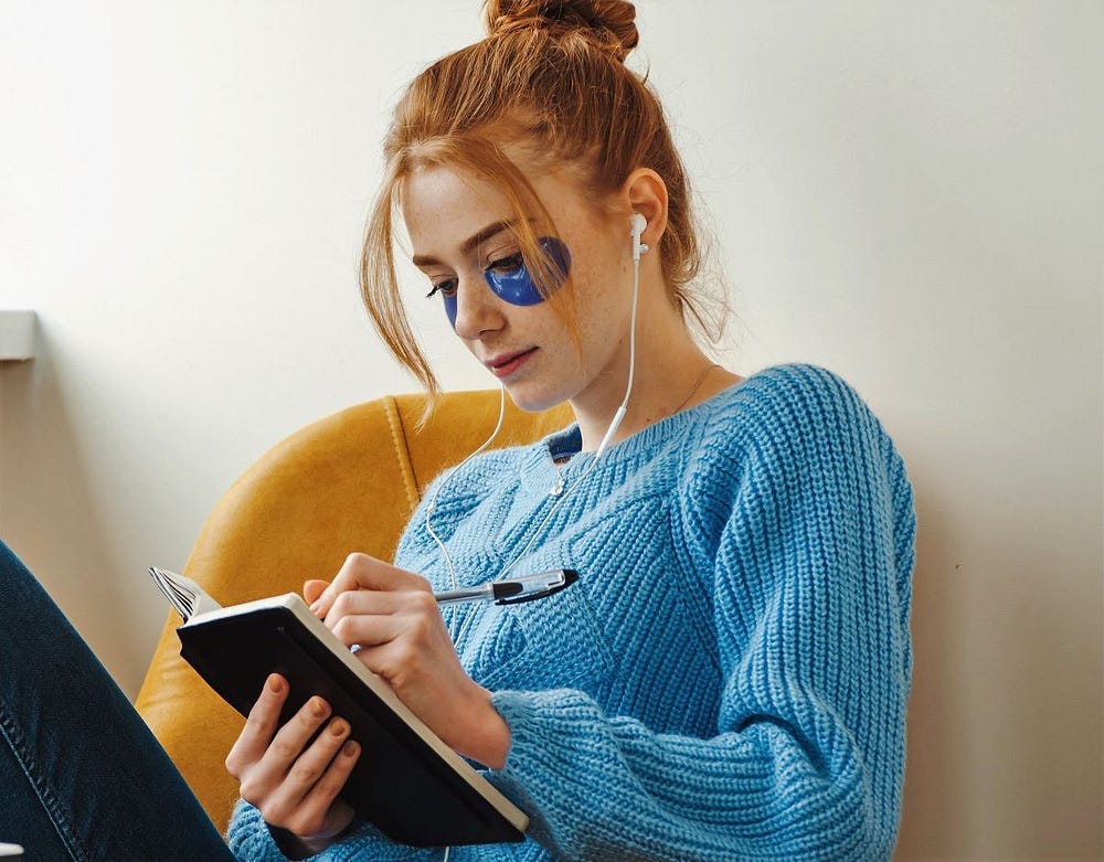 A young with red hair and a blue jumper woman is writing in a notepad. A young with red hair and a blue jumper woman is writing in a notepad.