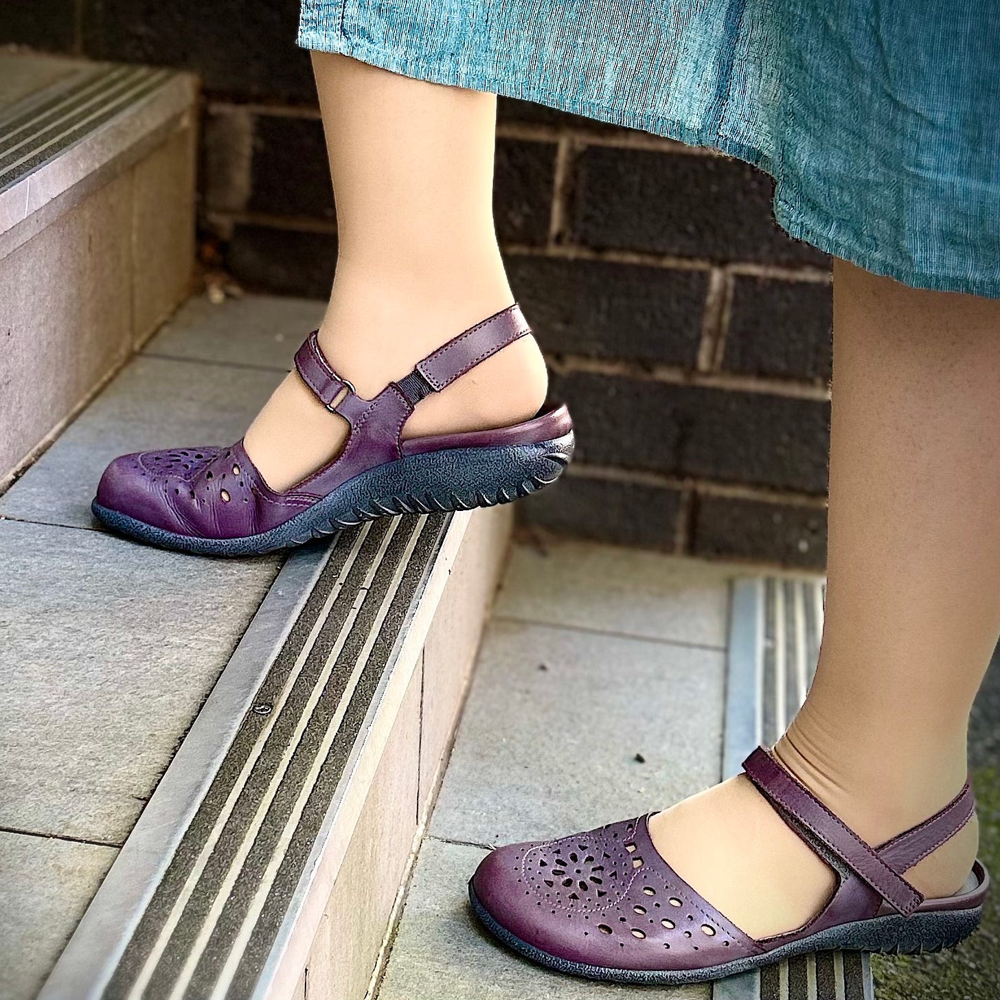 Photo of the author's feet, clad in purple sandals, going up gray tiled steps against a brown brick background.