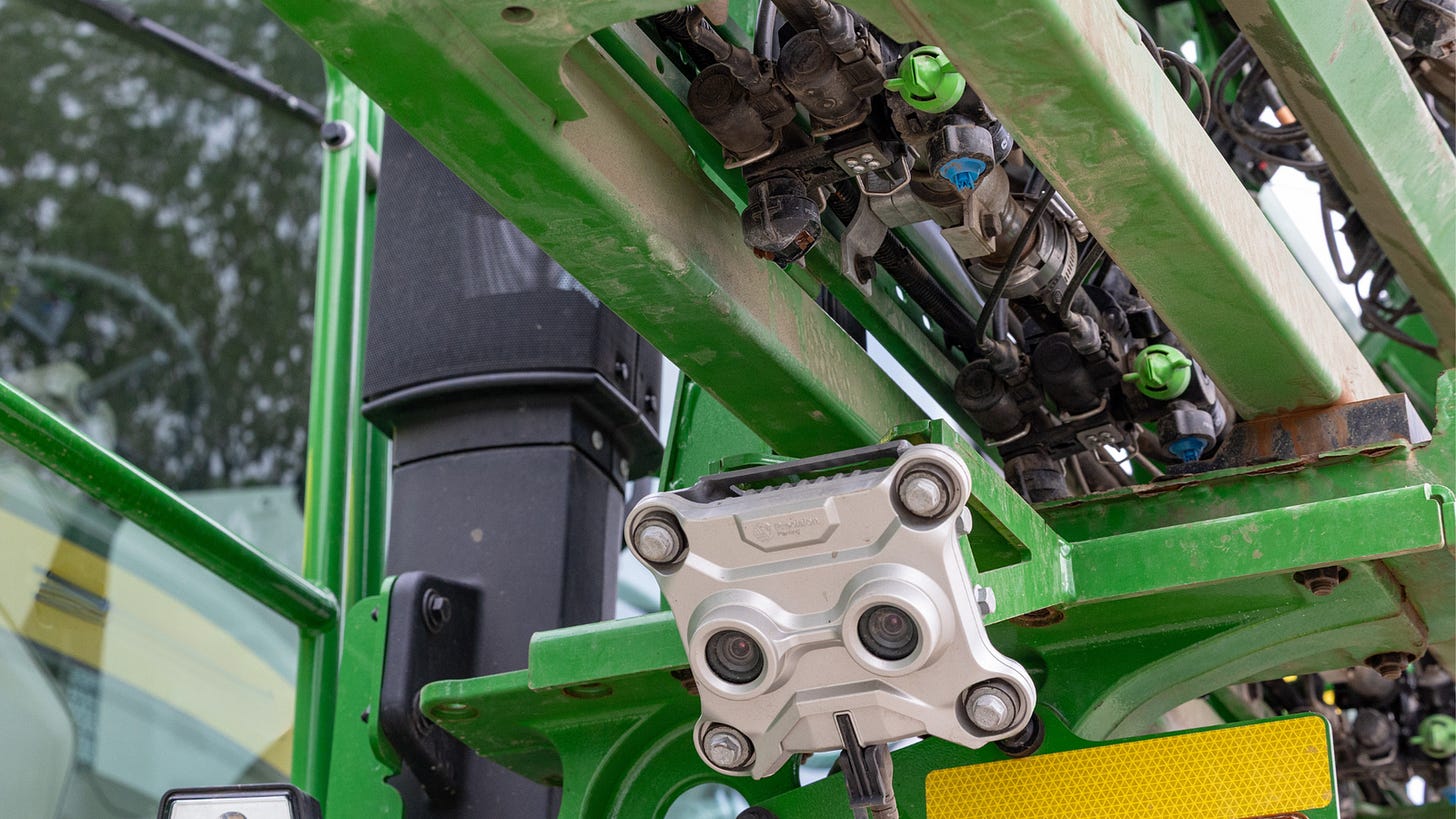 Close-up photograph of SymphonyVision Duo camera and sprayer nozzles mounted underneath a John Deere boom.