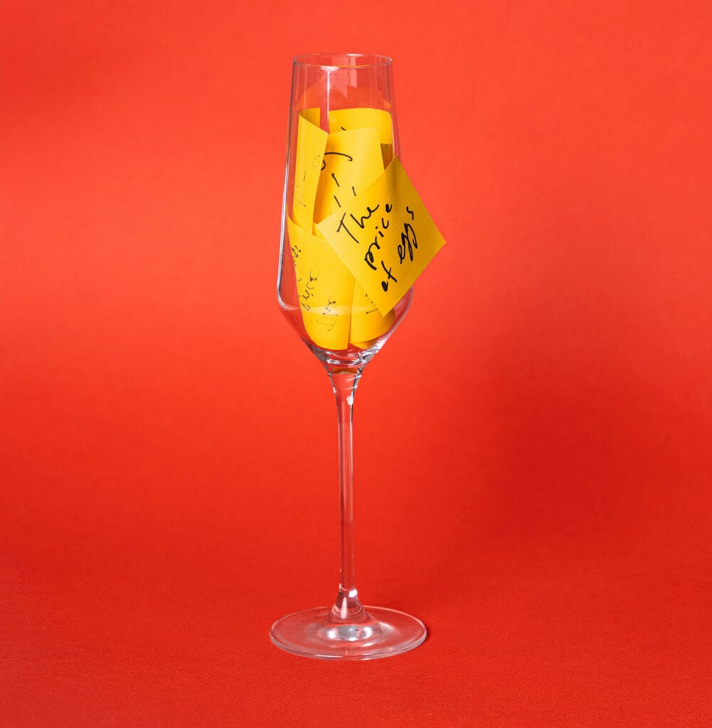 A champagne flute stuffed with yellow Post-it notes with recently popular words and phrases written on them. One note, with “the price of eggs” on it, is stuck to the outside of the glass.  