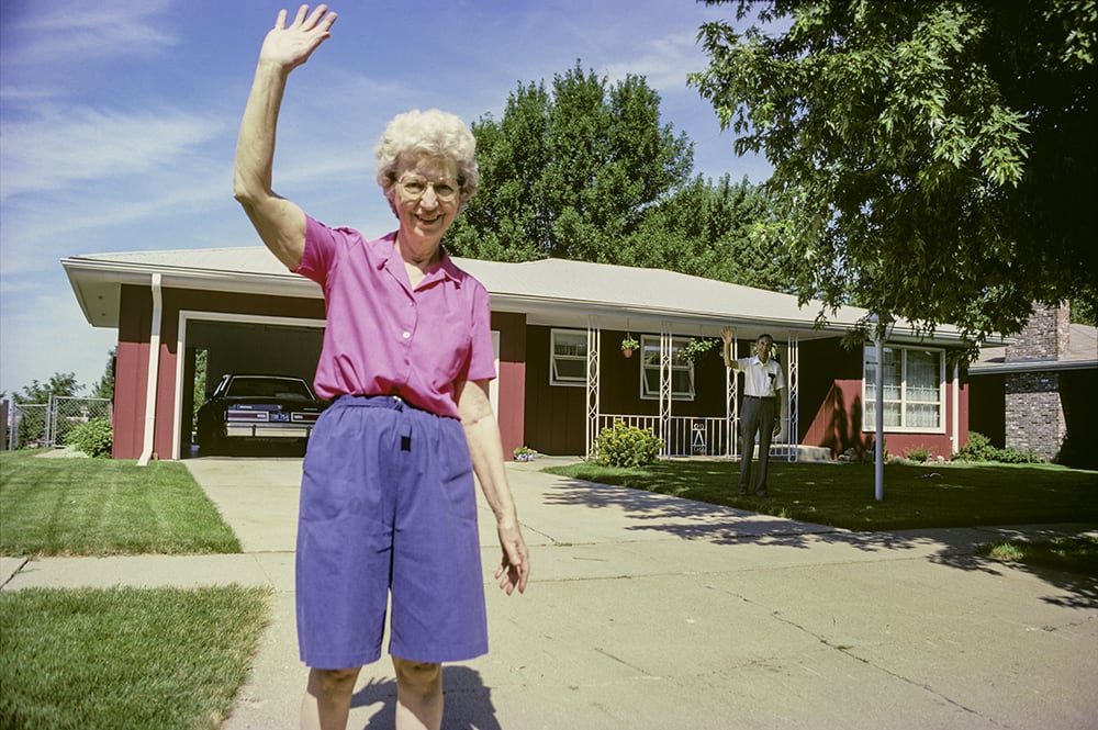 A person waving in front of a house

Description automatically generated