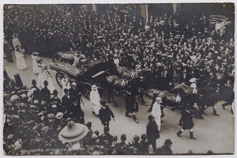Black and white photo of a large crowd attending a funeral procession featuring a horse-drawn carriage, with individuals in formal attire, circa 1913.