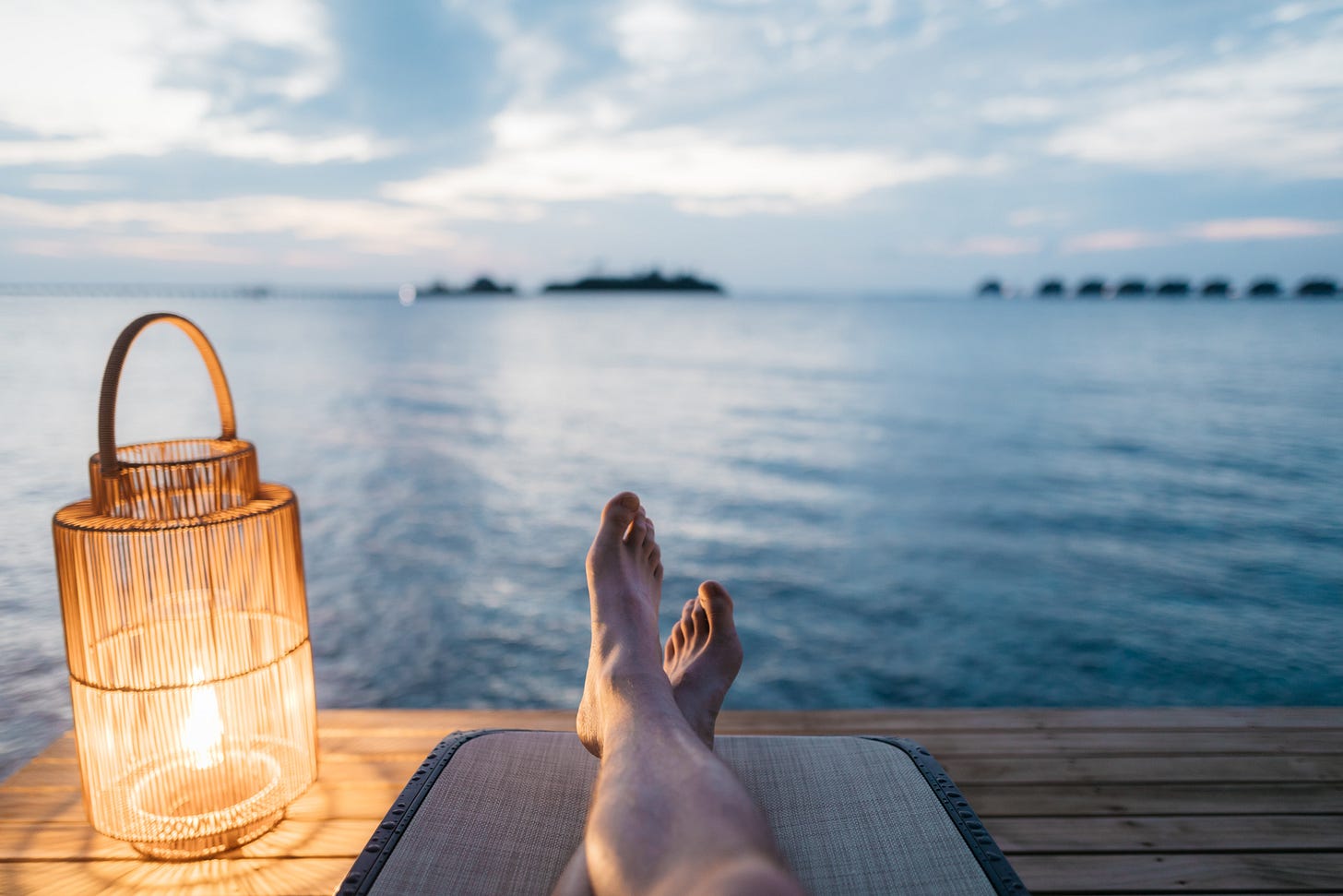 A person sitting by the sea on a pier next to a lantern A person sitting by the sea on a pier next to a lantern