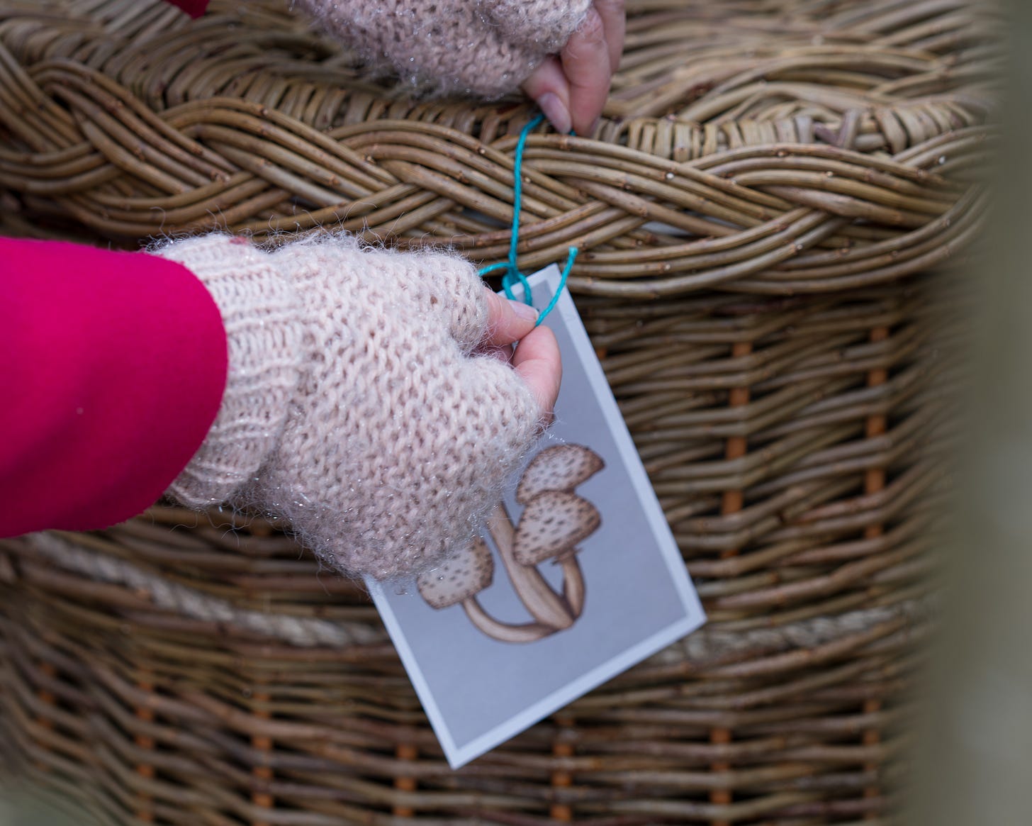 a pair of hands in fingerless gloves tying a mushroom postcard onto a willow coffin.