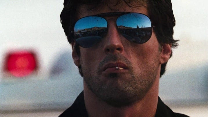 Sylvester Stallone sunglasses close-up in Cobra 4K UHD – Matchstick-chewing Stallone in reflective aviators, from the Arrow Video 4K Dolby Vision presentation.