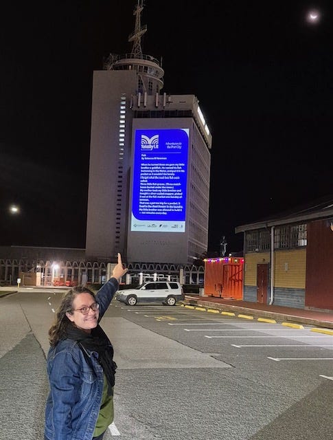 Rebecca is pointing to a building where her 100-word story 'Fish' has been projected at night.