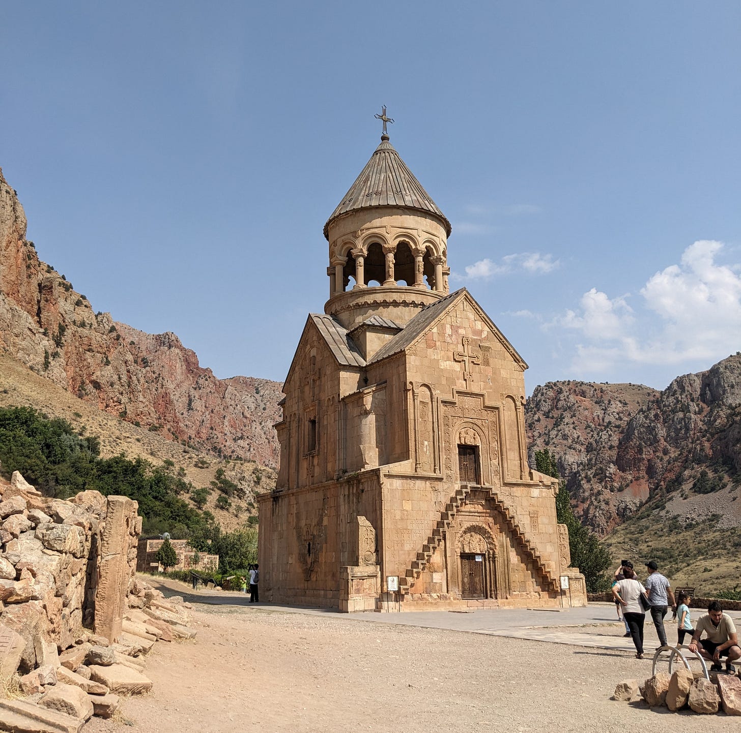 A pale stone church with a spire an large arched doorway, surrounded by a rocky mountain landscape with bright blue sky. 