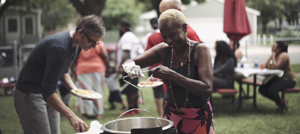 People stand together enjoying food in someone's front yard.