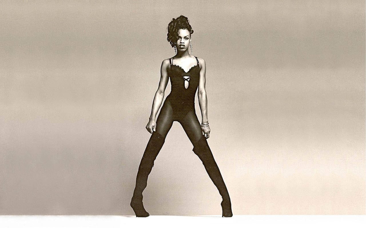 A picture of model Connie Fleming, wearing a black body stocking and high-heeled boots, posing dramatically in a photo studio environment.