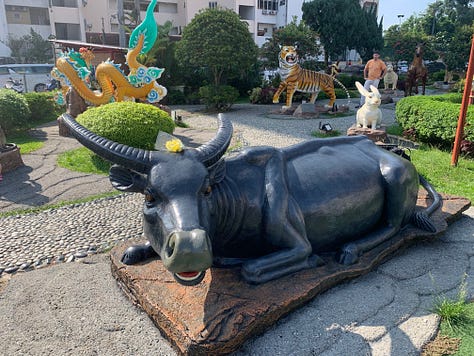 Two children aged 2 and 4 throw flowers into a fountain at a Chinese temple; red lanterns hang overhead at Thean Hou temple; a statue of an oxen in the garden at the temple.