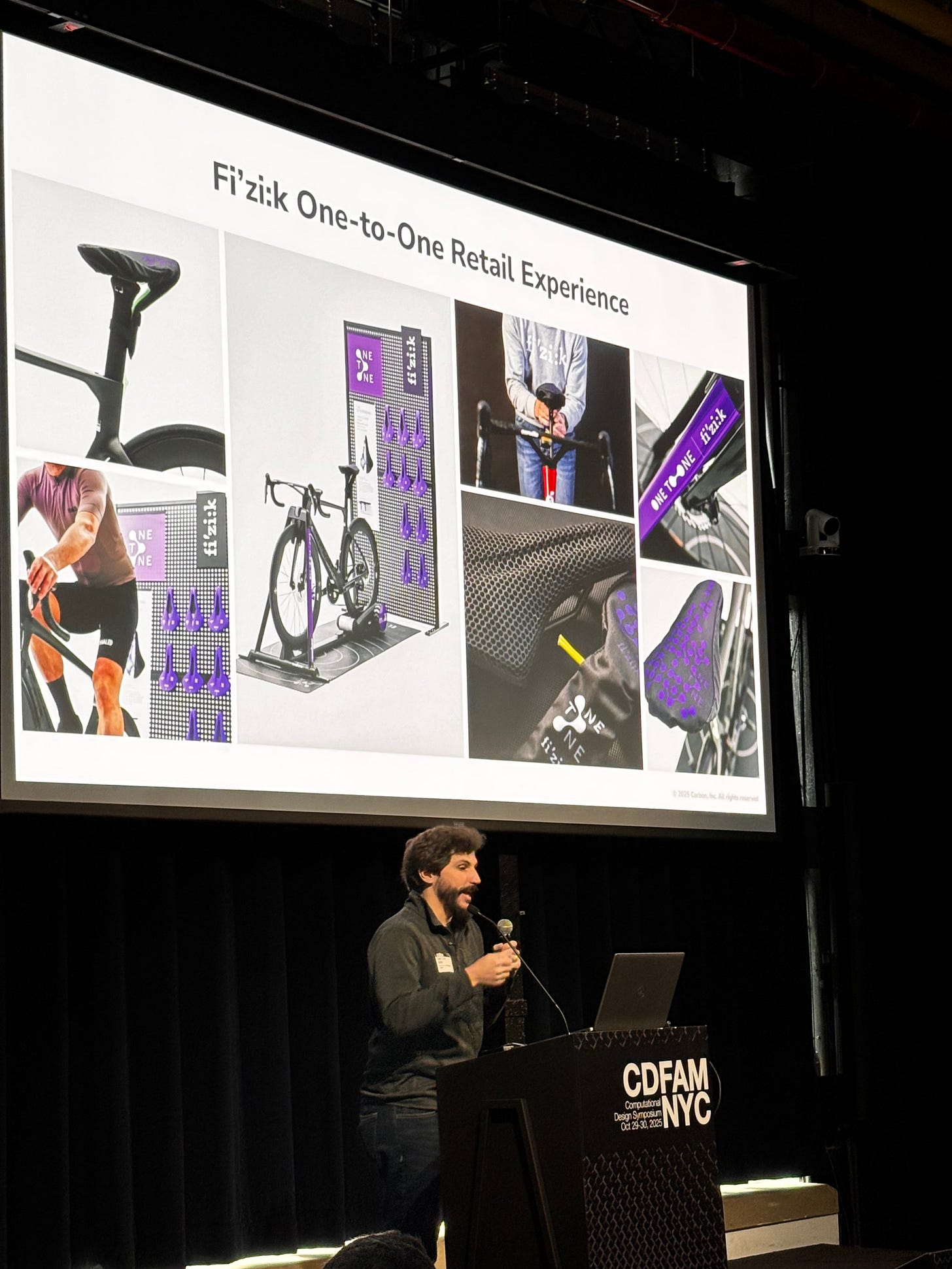 Andrew Sink of Carbon presenting at the CDFAM NYC 2025 event, with a large screen behind them displaying the Fi'zi:k One-to-One Retail Experience, featuring images of bicycle components and a retail setup. Andrew Sink of Carbon presenting at the CDFAM NYC 2025 event, with a large screen behind them displaying the Fi'zi:k One-to-One Retail Experience, featuring images of bicycle components and a retail setup.