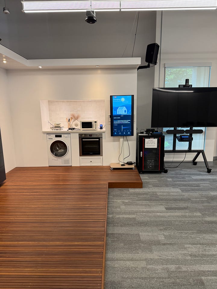 A photo of a vertical, black home battery, and a wide image showing a showroom kitchen with a large screen displaying energy usage statistics.