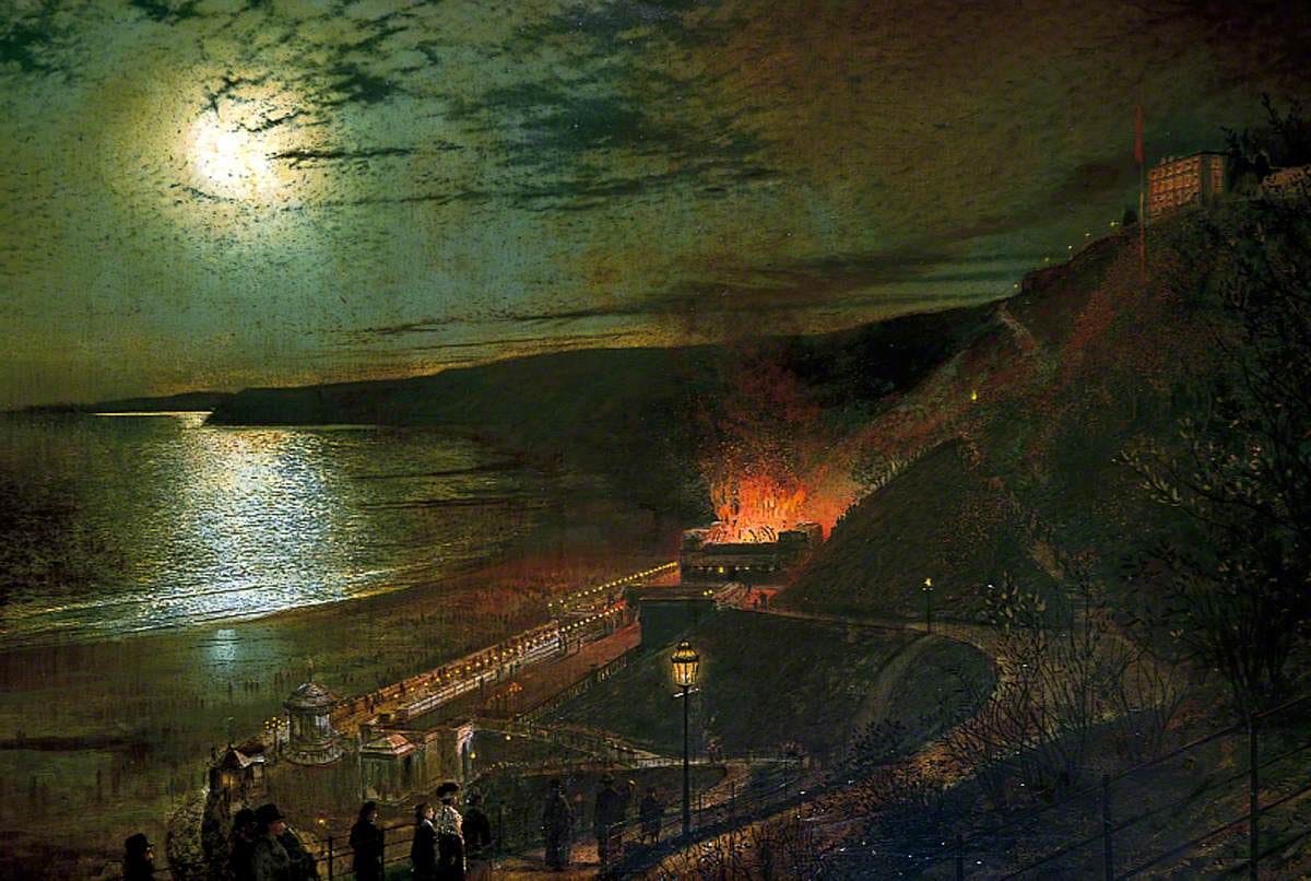 Seen from a cliff path at night, a building on the seafront burns below while spectators watch from the railings and a full moon shines on the bay.