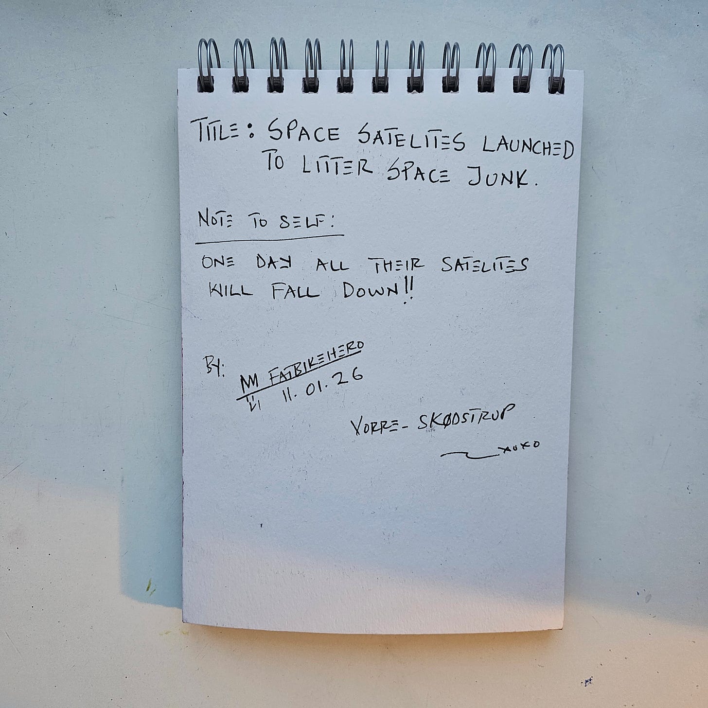 Alt Text: The back of a sketchbook page containing handwritten notes by FatbikeHero. The title reads "TITLE: SPACE SATELITES LAUNCHED TO LITTER SPACE JUNK." A note below reads "NOTE TO SELF: ONE DAY ALL THEIR SATELITES WILL FALL DOWN!!" Signed "M FatbikeHero," dated "11.01.26," and located at "Vorre-Skødstrup." Alt Text: The back of a sketchbook page containing handwritten notes by FatbikeHero. The title reads "TITLE: SPACE SATELITES LAUNCHED TO LITTER SPACE JUNK." A note below reads "NOTE TO SELF: ONE DAY ALL THEIR SATELITES WILL FALL DOWN!!" Signed "M FatbikeHero," dated "11.01.26," and located at "Vorre-Skødstrup."