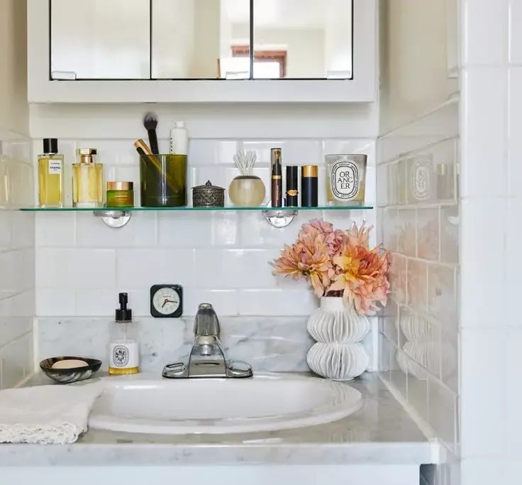 This may contain: a bathroom sink sitting under a mirror next to a white cabinet and counter top with flowers on it
