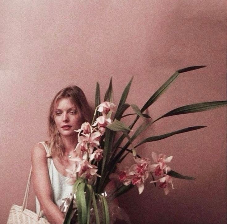 This may contain: a woman sitting on the floor with a basket and flowers in front of her,