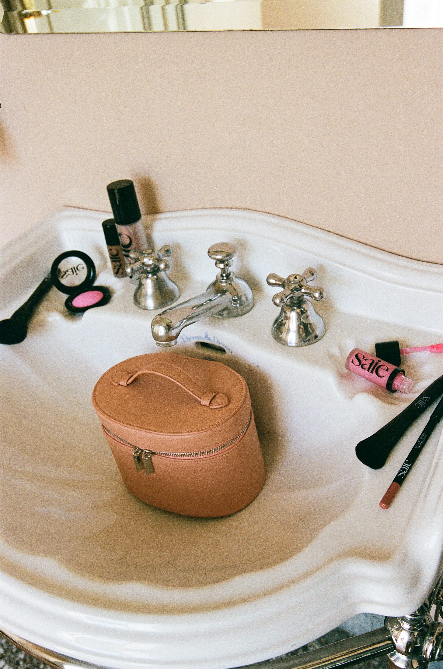 A bathroom sink with a Saie makeup bag and makeup scattered around the sink.