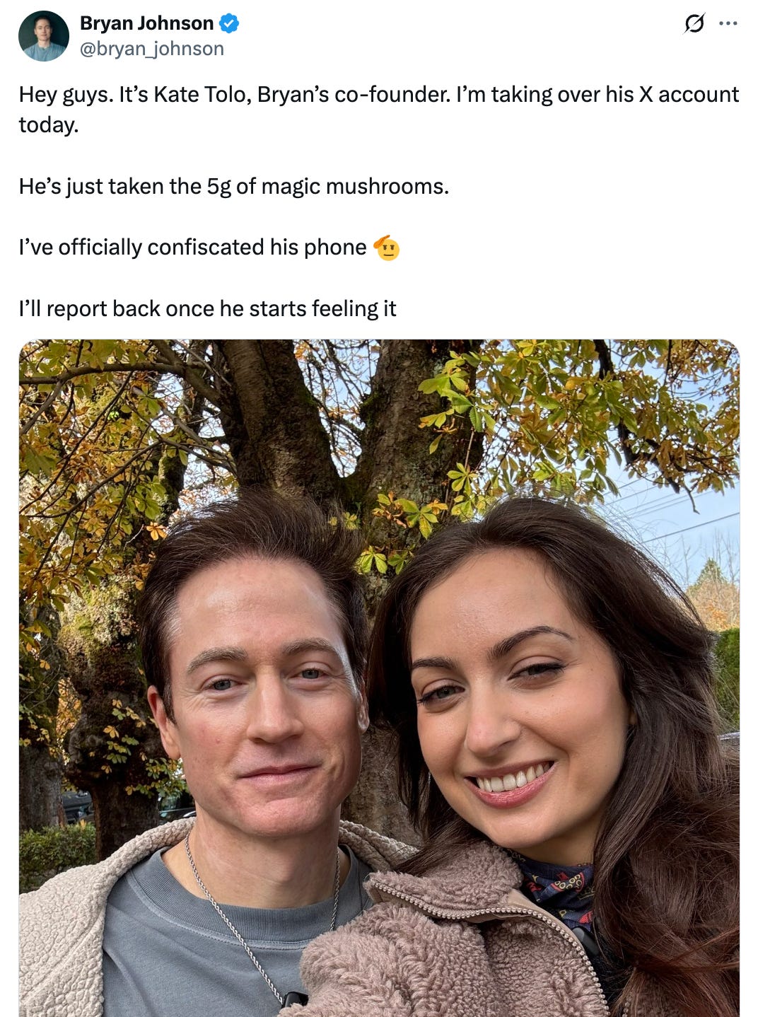 Tweet from @bryan_johnson that says, "Hey guys. It’s Kate Tolo, Bryan’s co-founder. I’m taking over his X account today.   He’s just taken the 5g of magic mushrooms.  I’ve officially confiscated his phone 🫡  I’ll report back once he starts feeling it" and features an image of him and a smiling brunette woman