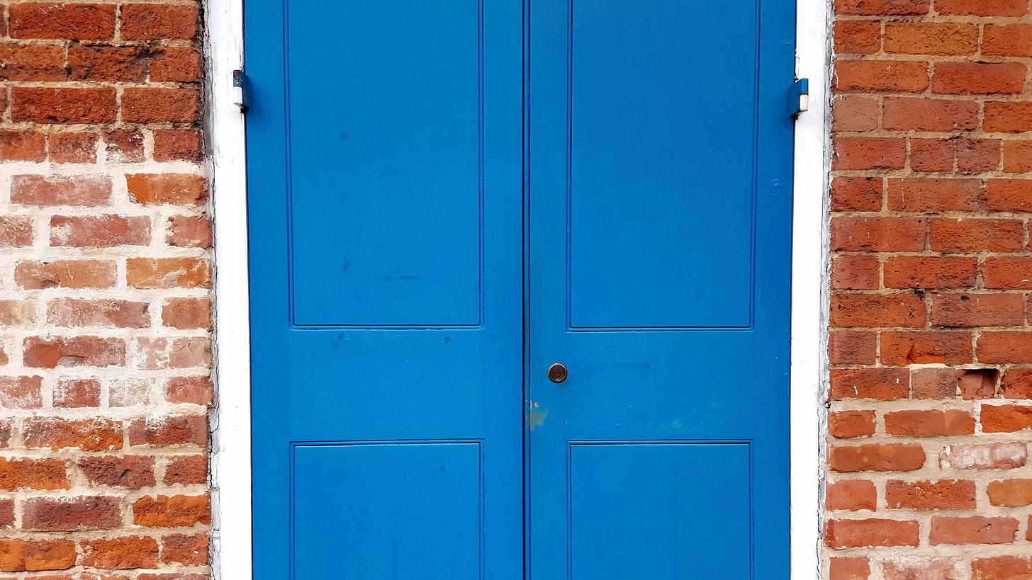 A bright blue double-door closed and surrounded by a red brick wall