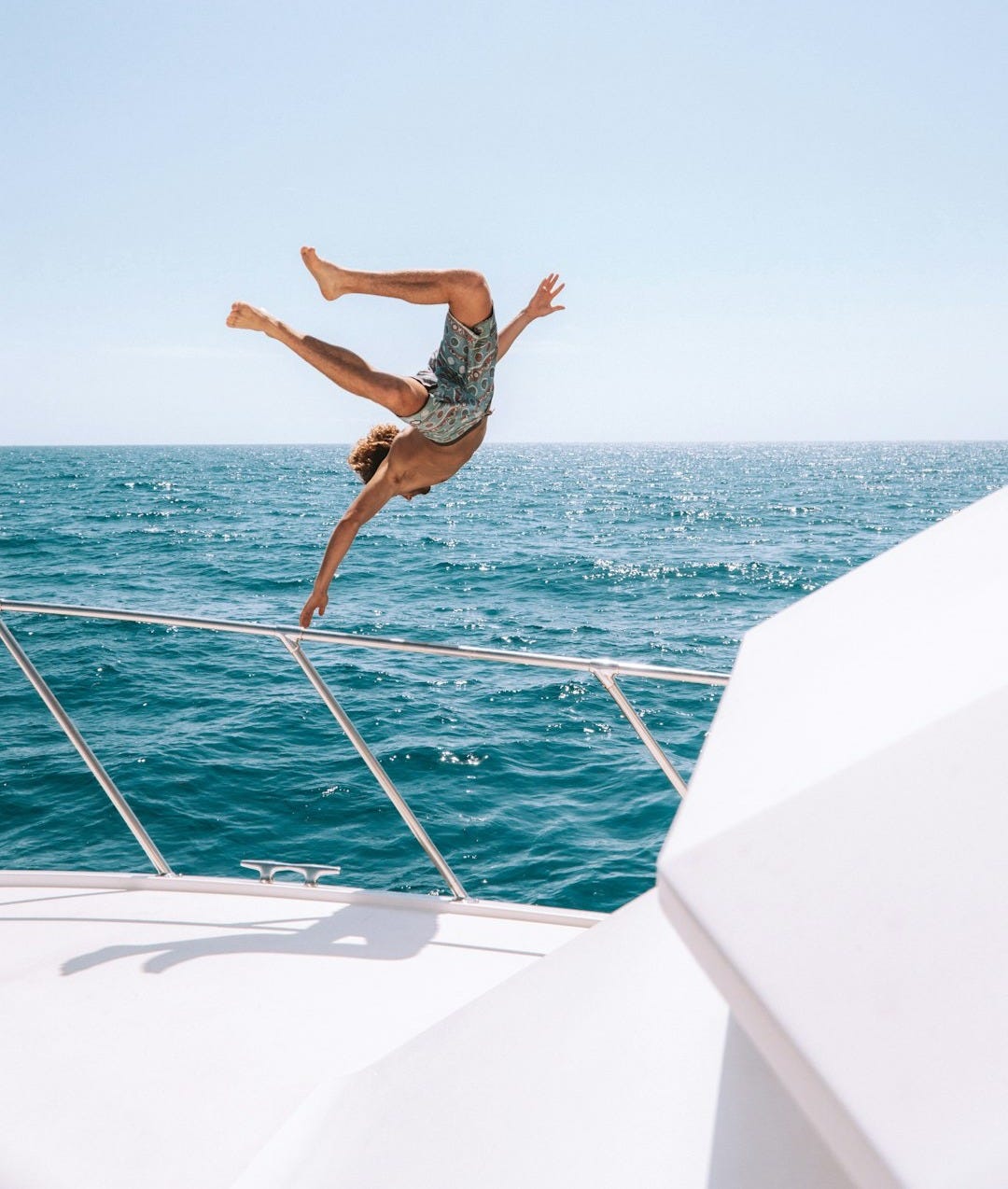 man in black shorts jumping on white boat during daytime