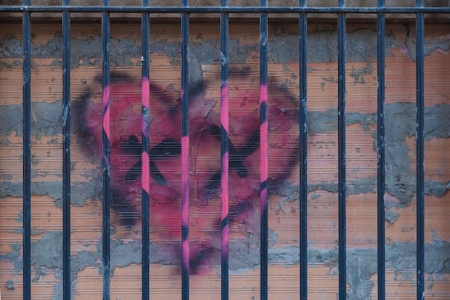 Graffiti heart with two Xs on a fence and brick wall, symbolizing betrayal and lost trust.