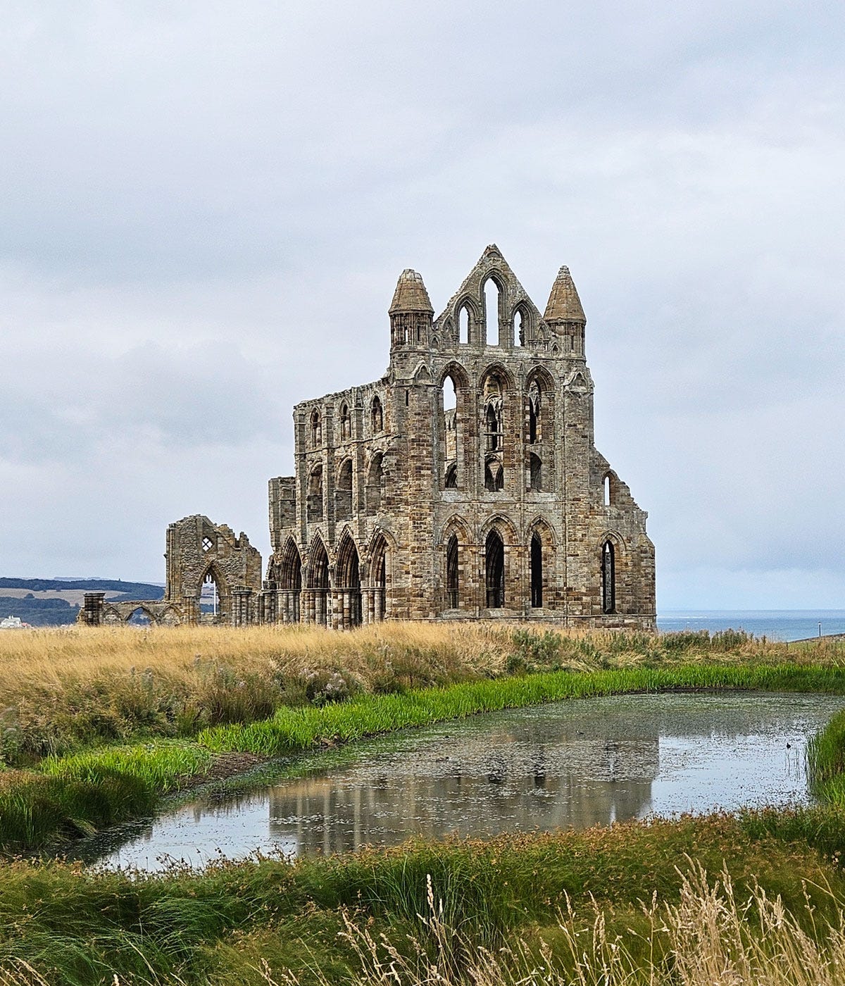Long distance view of a ruined building, reflected in a creek in front of it