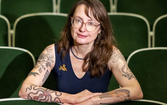 emily wilson sitting very stiffly in a movie theater seat with a look on her face that's like "well, ACTUALLY..."