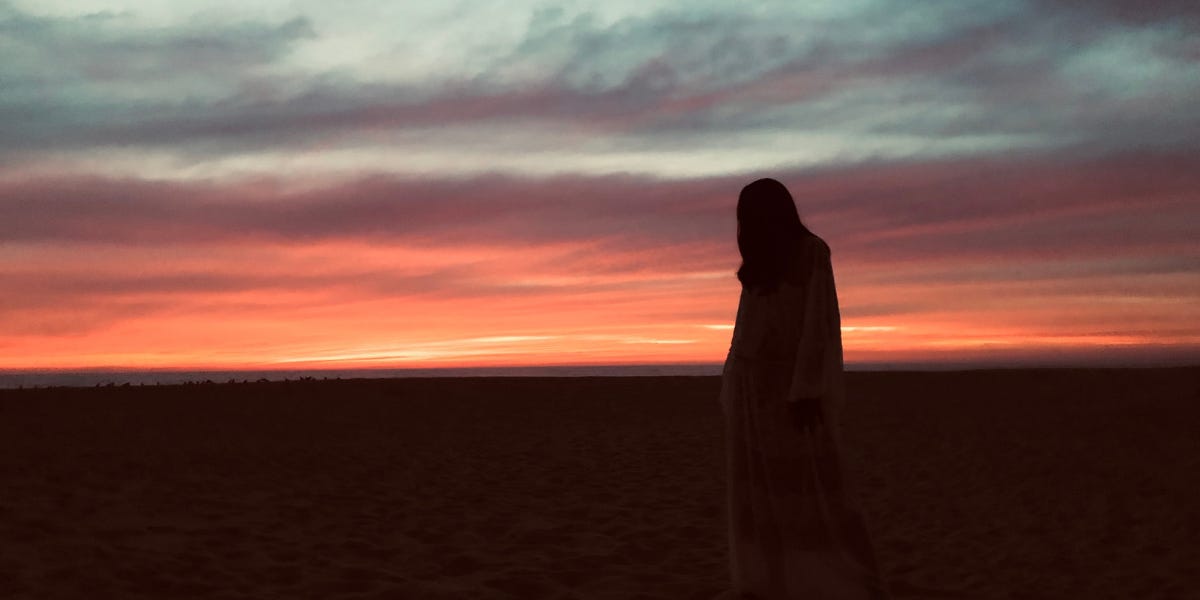 a silhouette of a person standing on the beach at sunset