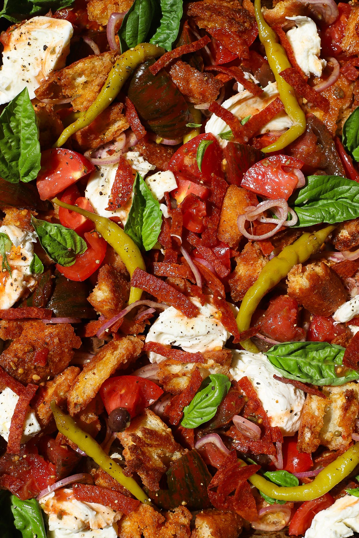 Close-up of panzanella with crispy pepperoni, tomatoes, mozzarella, green peppers, and basil leaves