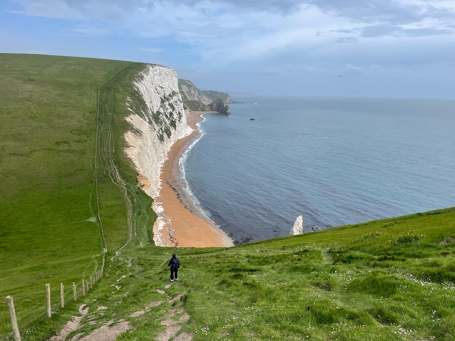 Hiker walking downhill on a grassy seaside slope Hiker walking downhill on a grassy seaside slope