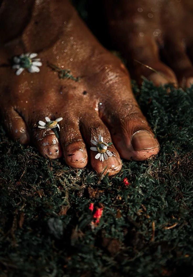 This may contain: a person's feet covered in mud with flowers on their toe and toes, surrounded by green grass