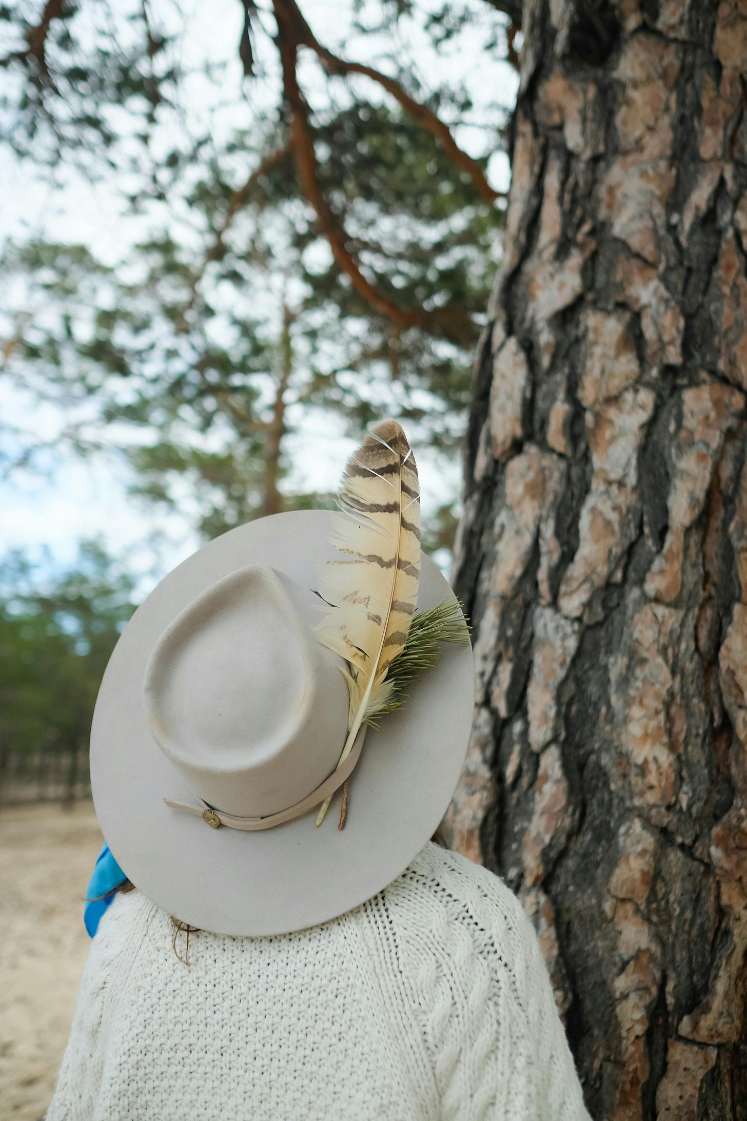 A person in a hat with a feather in it in front of a tree.