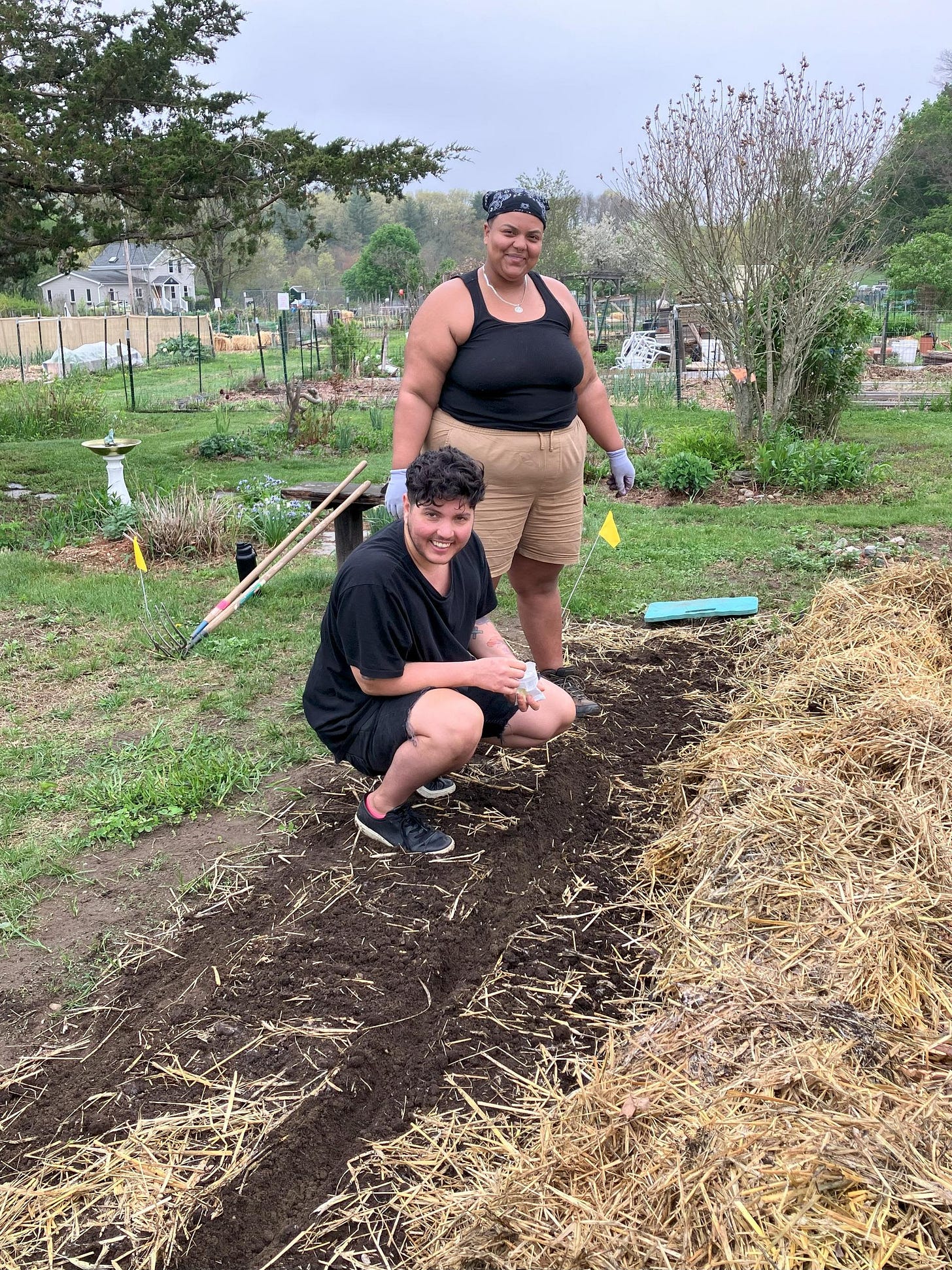 Shai and Mr J are smiling in a garden patch covered with hay.