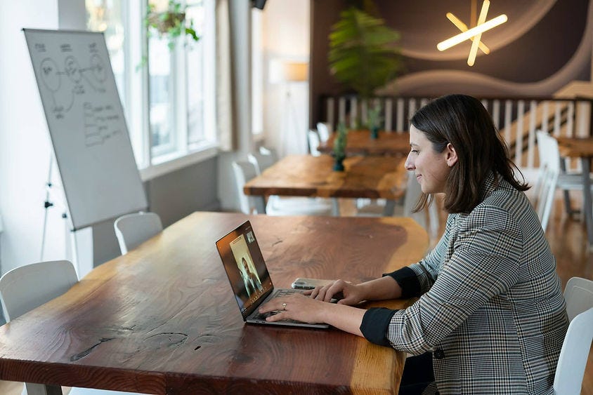 A woman typing on laptop on table and there is a whiteboard on the left
