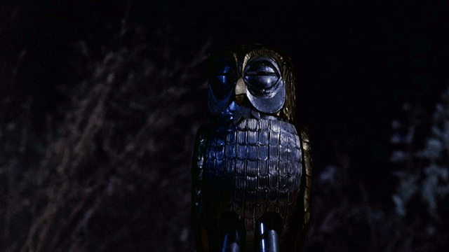 A mechanical silver owl squints eyes and turns head side to side infront of swaying trees, a gif of bubo the owl from Jason and the argonaughts mid century film