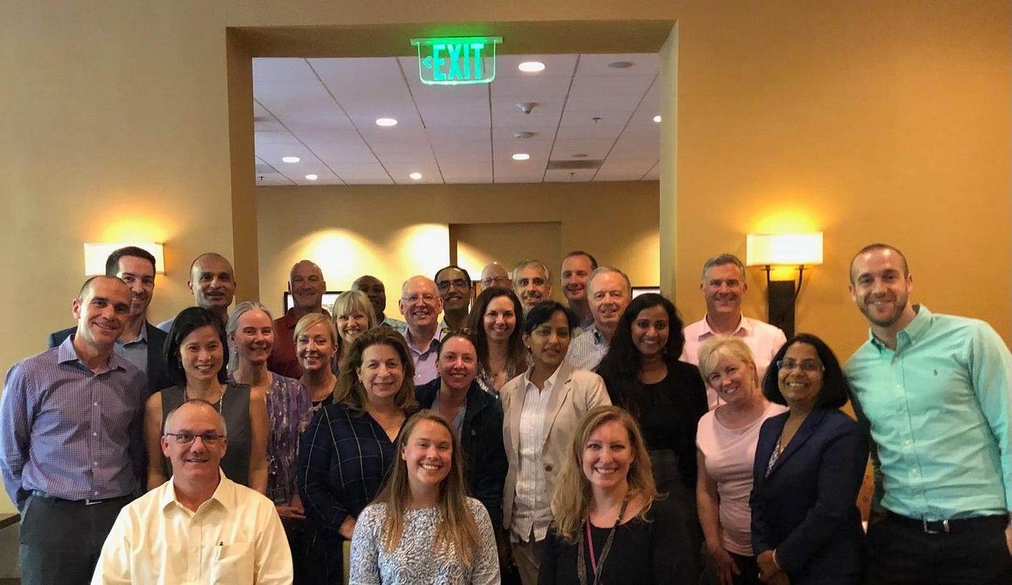 Group of corporate coworkers posing for a photo with an exit sign overhead.
