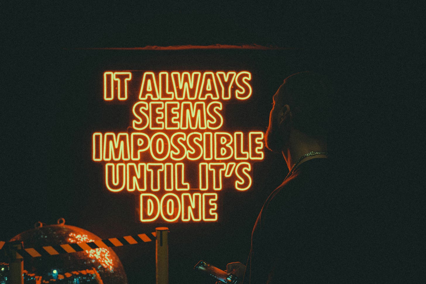 neon sign in orange block letters that reads "It always seems impossible until it's done." neon sign in orange block letters that reads "It always seems impossible until it's done."