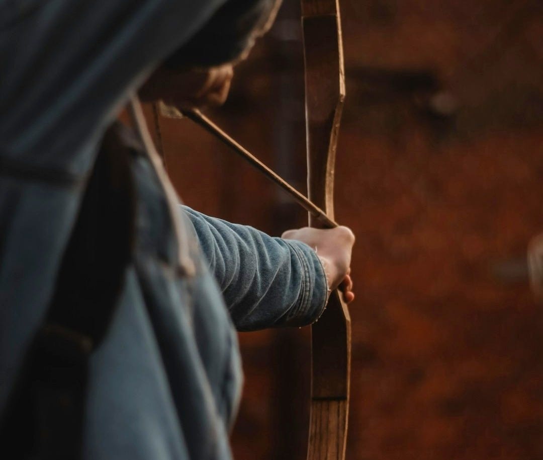 a person holding a bow and aiming it at something a person holding a bow and aiming it at something