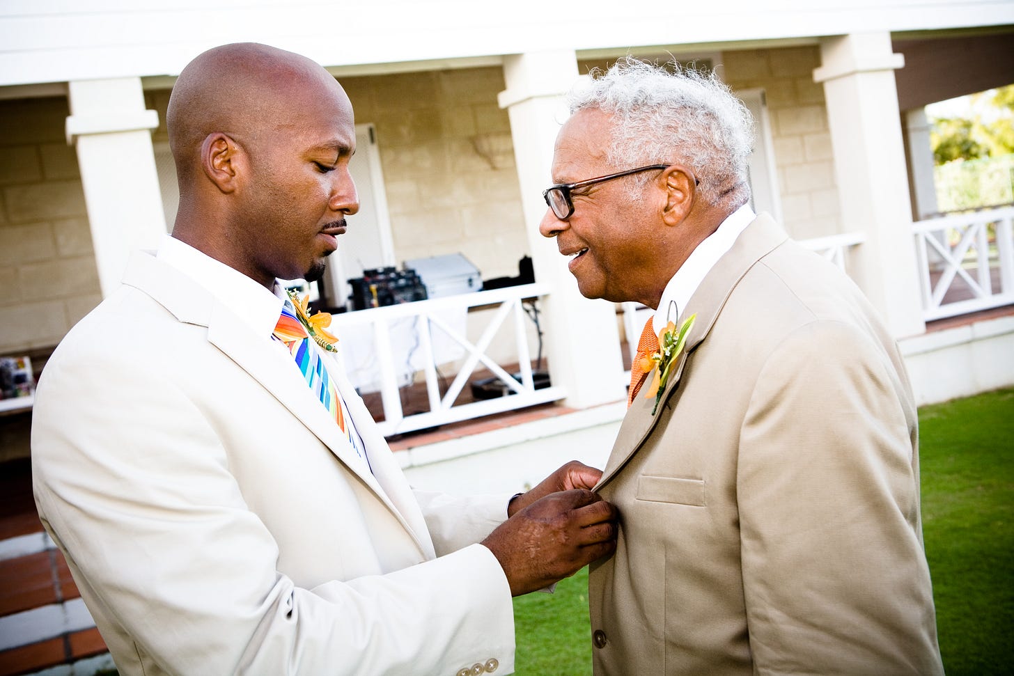 A father and son where the son is on the left helping the father with his jacket and the father is laughing.