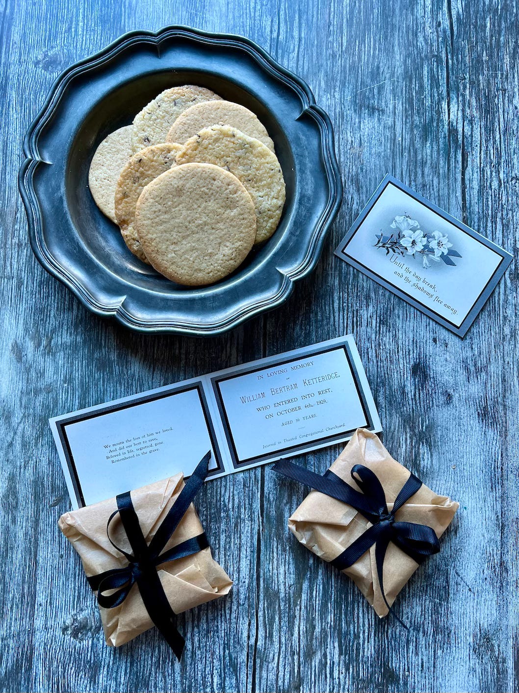 Biscuits on a pewter plate and some wrapped in parcels with tied with black ribbon plus a funeral card