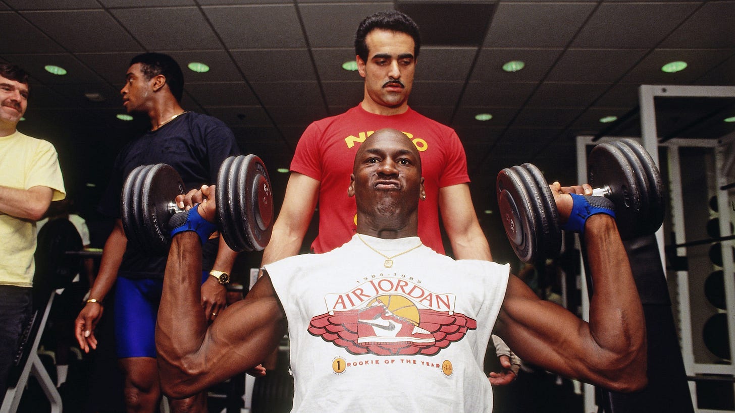 Michael Jordan lifting weights with a trainer spotting him behind