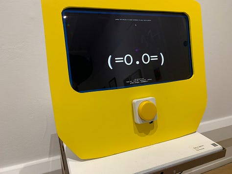 A variety of new media art works using screens, projections, including a large yellow screen and an anaologe cassete with the caption "an actual AI artist" 