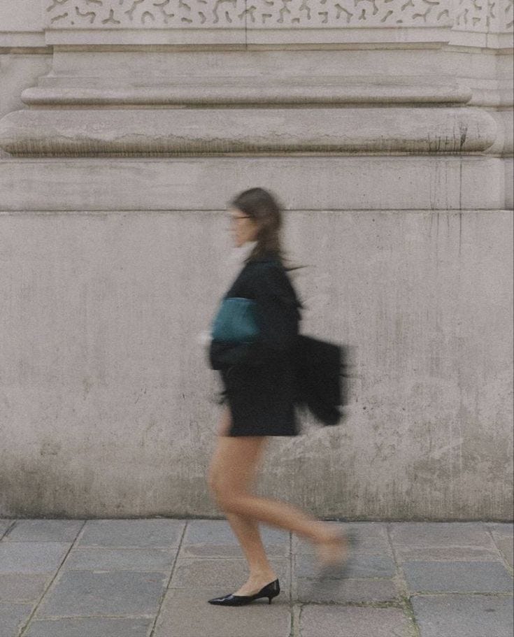 This may contain: a woman walking down the street with a backpack on her back and shoes in front of her