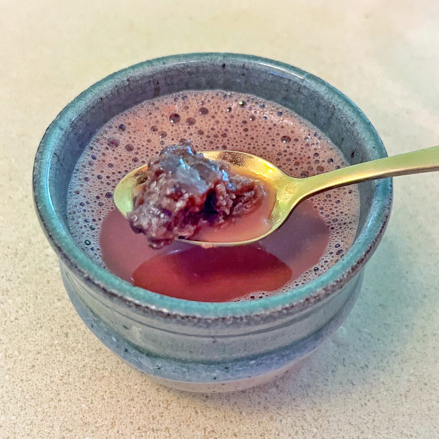 A chunk of kūlolo in a gold spoon hovering over a cup of hot chocolate