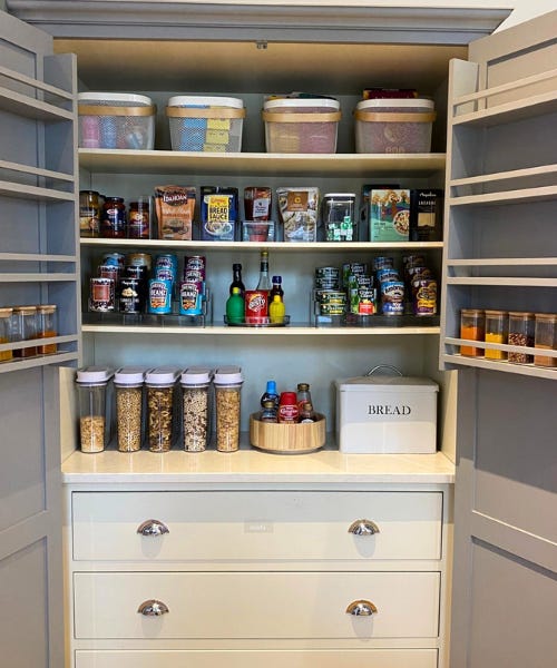 An open kitchen storage cupboard with grains, cans, and tea bags inside