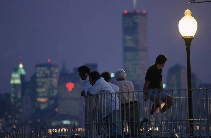 This may contain: some people are standing on a bridge looking at the city lights and skyscrapers in the distance