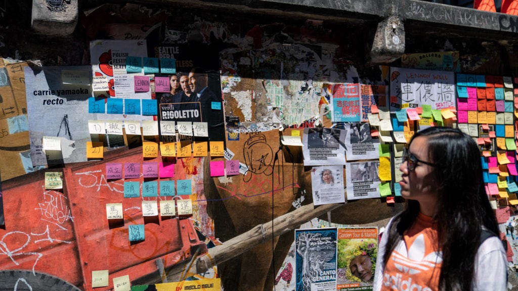 A woman looks at a wall in the street, covered with sticky notes