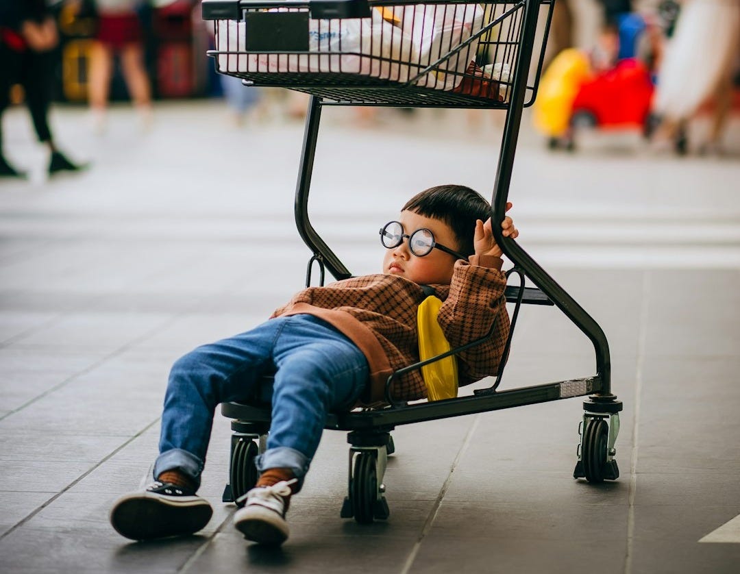 boy in orange jacket sitting on black shopping cart