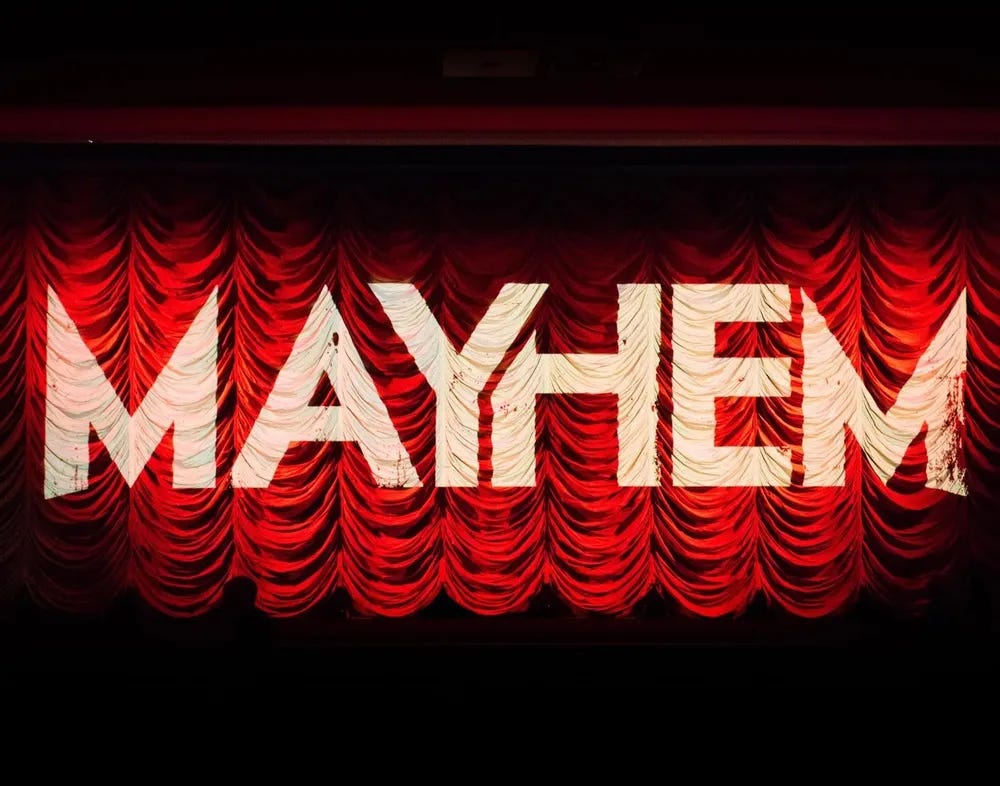 A photo of the curtain in front of the screen in Broadway Cinema's Screen One. The Mayhem logo, in white, is projected against the red curtains.