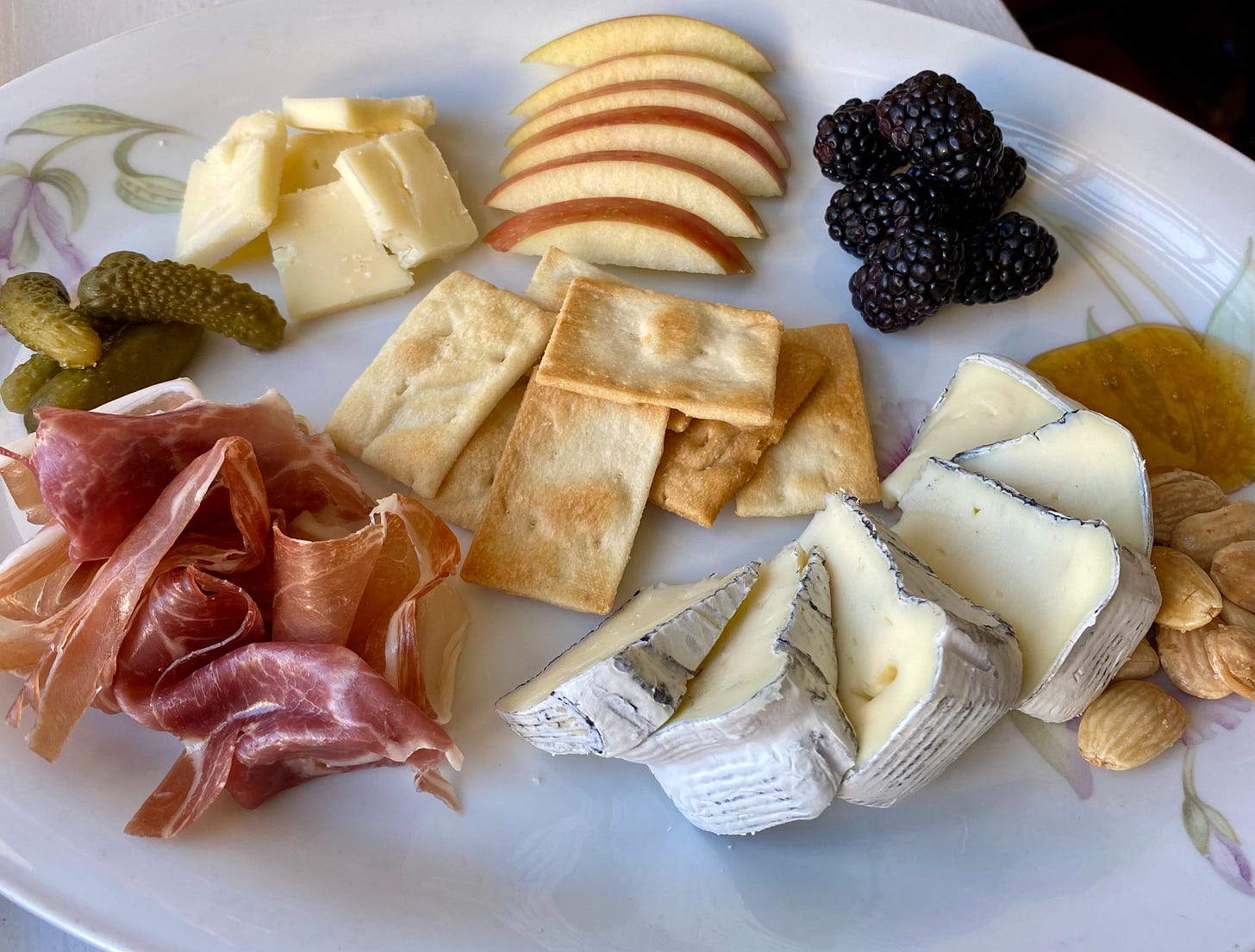 cheese plate with olive oil crackers in the middle surrounded by (clockwise from top) red apple slices, blackberries, honey, marcona almonds tucked behind slices of Dorothy's Keep Dreaming cheese, prosciutto, cornichons, and Milton Creamery's Prairie Breeze cheese
